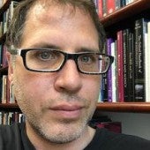 a headshot-style picture of Timothy Schroeder, with a bookshelf in the background